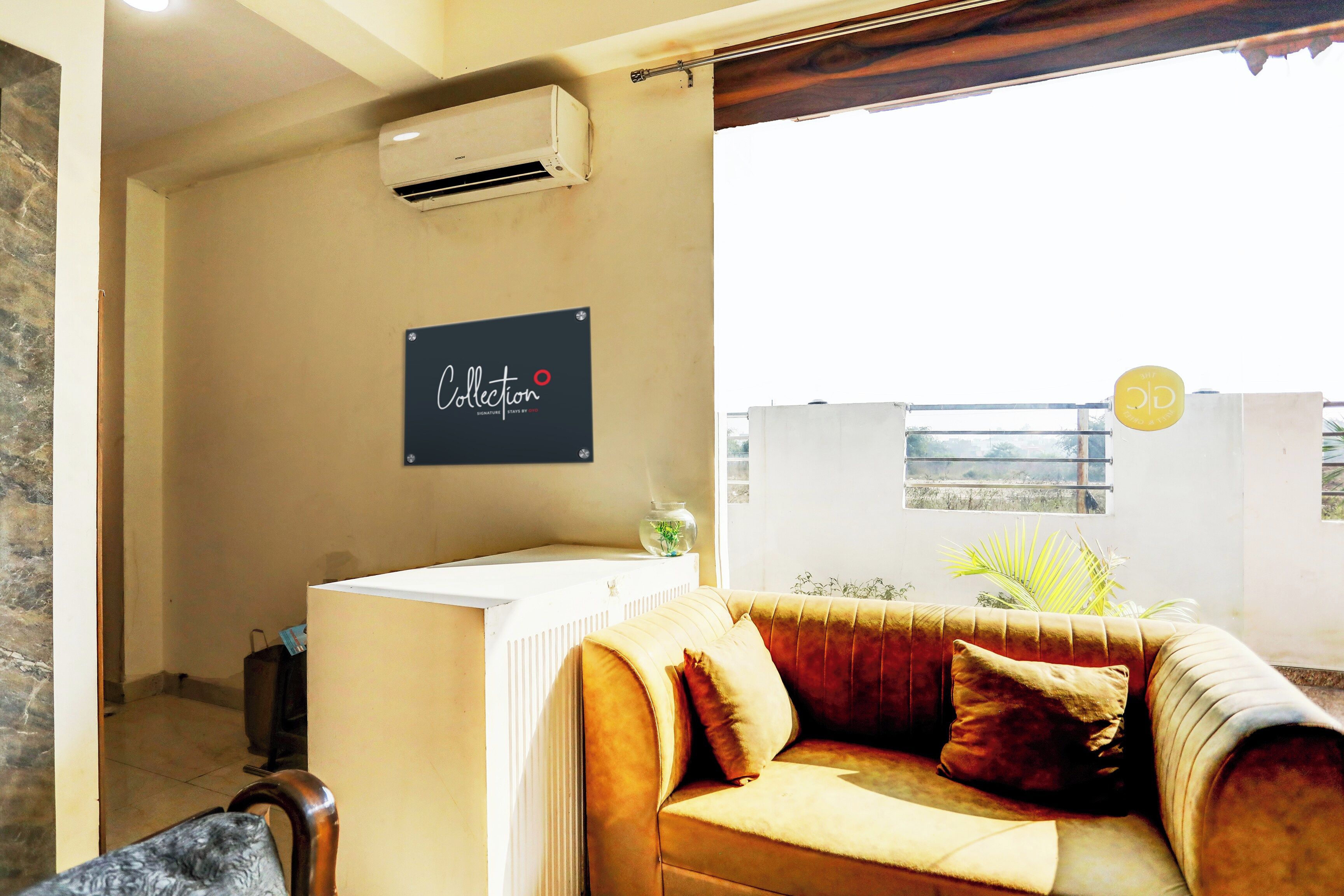A room with a beige sofa, a small table with a vase, and a wall-mounted air conditioner.