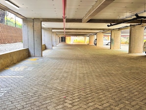 An indoor parking area with concrete pillars, a tiled floor, and a clear view of the outside.