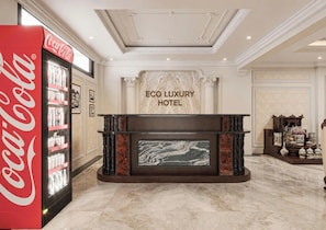 A lobby with a Coca-Cola vending machine, a fireplace with a marble surround, and a sign reading 'ECO LUXURY HOTEL'. - Eco Luxury Ha Noi Hotel  (Cau giay)