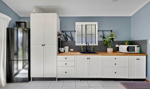 Une cuisine moderne avec des meubles blancs, un four à micro-ondes encastré et une fenêtre équipée de stores.