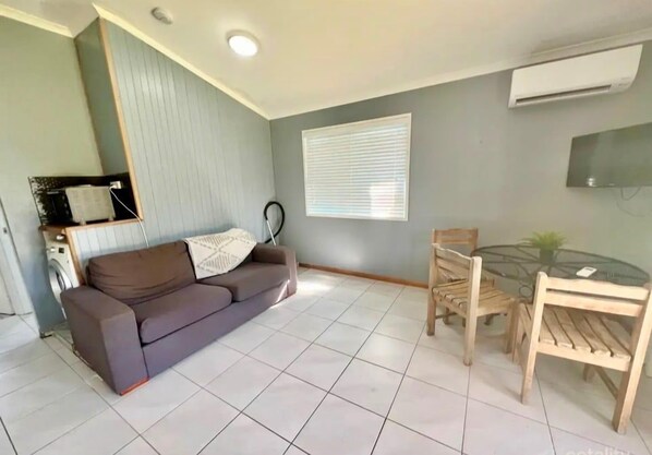 Un salon avec un canapé, une table à manger et des chaises, un lave-linge et un téléviseur fixé au mur.