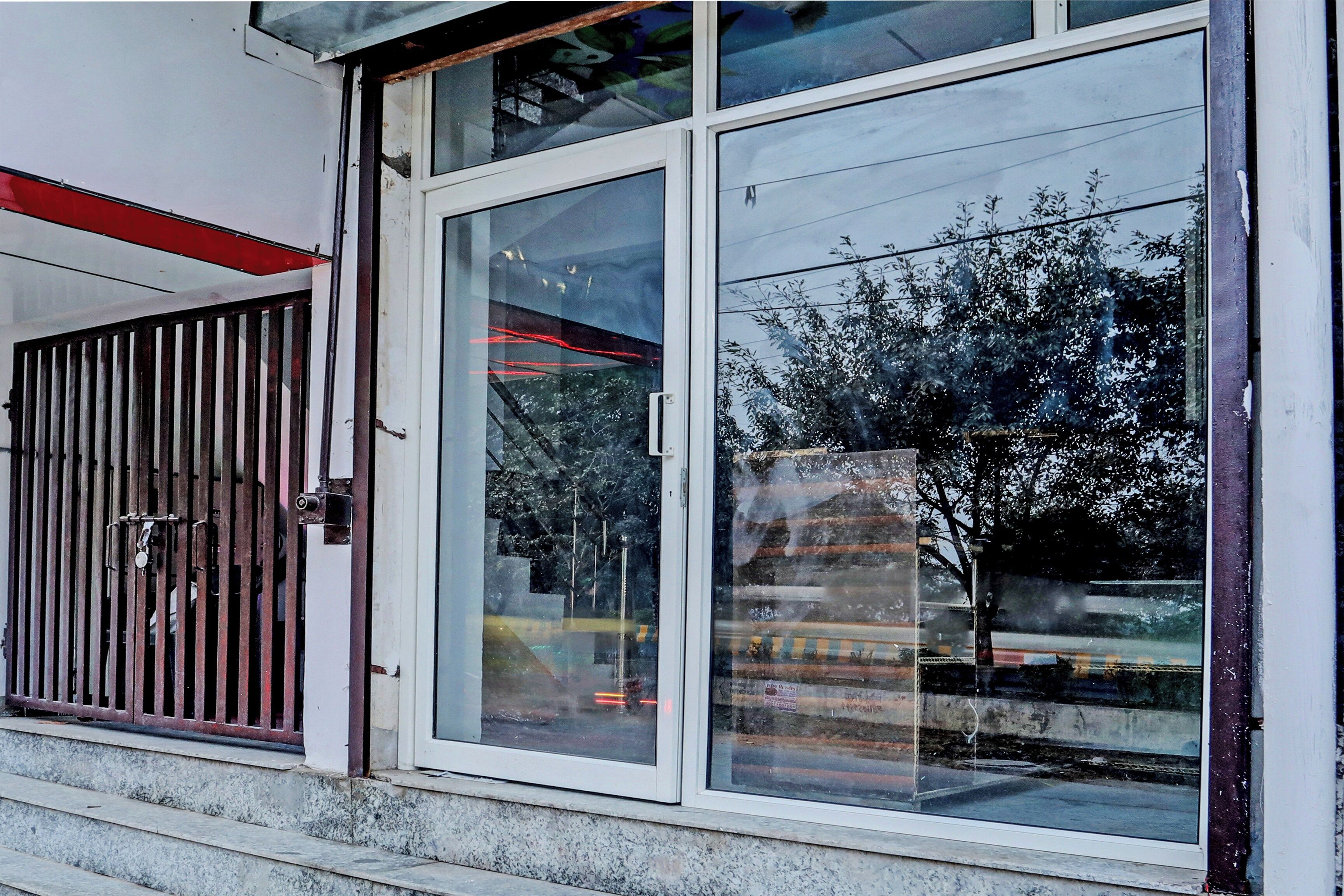 A building with a large window, a metal gate, and a reflection of a tree.