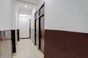 A corridor with a tiled floor leading to a door with a metal grille. - Hotel O shiva stay (Noida)