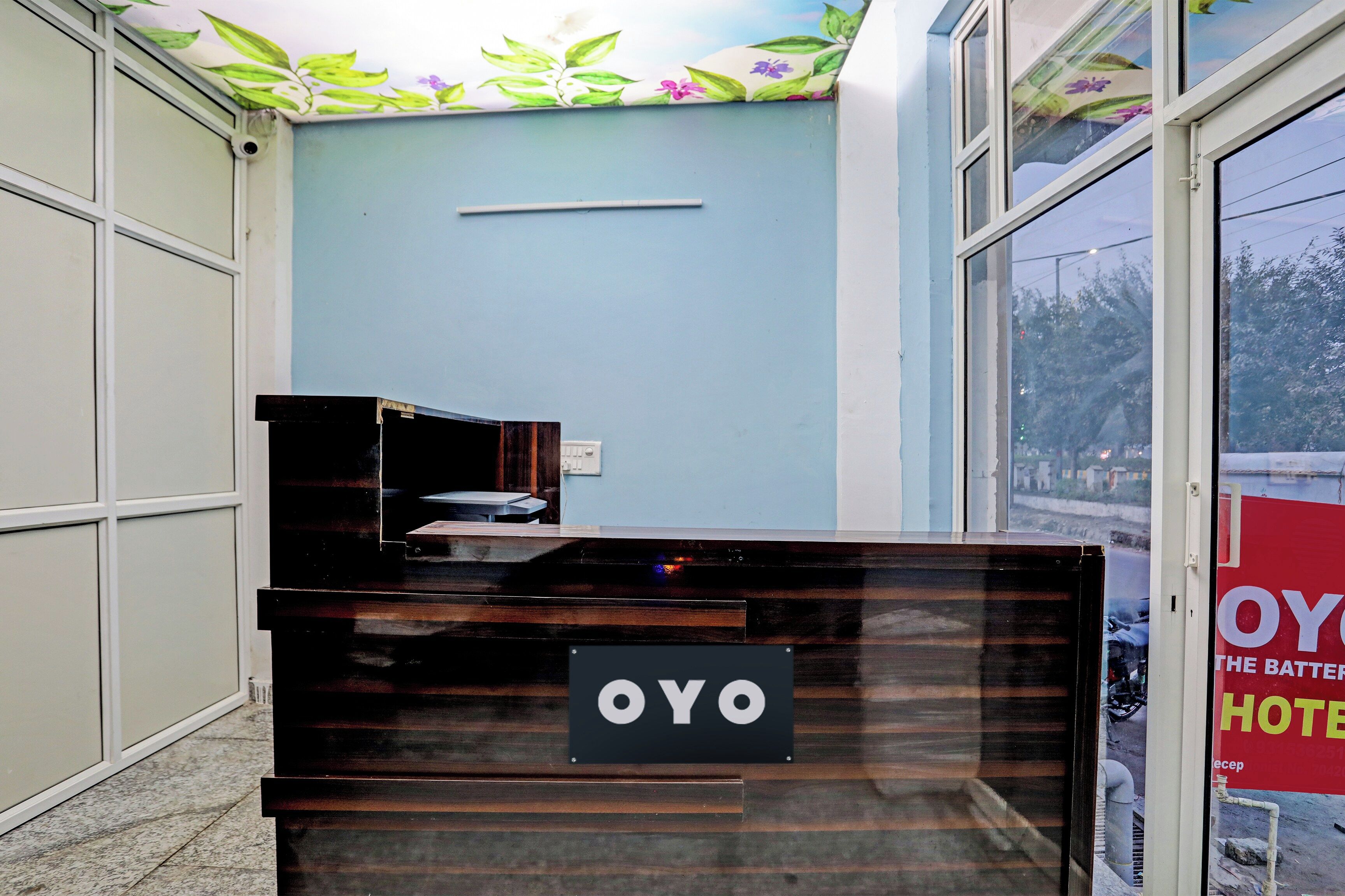 A reception desk with a sign that reads 'OYO HOTEL' in a hotel lobby with a blue wall and a window showing a street view.