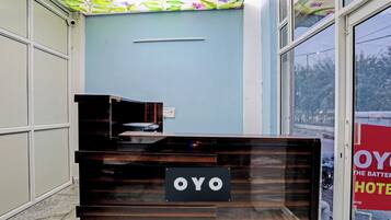 A reception desk with a sign that reads 'OYO HOTEL' in a hotel lobby with a blue wall and a window showing a street view.
