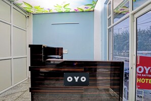 A reception desk with a sign that reads 'OYO HOTEL' in a hotel lobby with a blue wall and a window showing a street view. - Hotel O shiva stay (Noida)