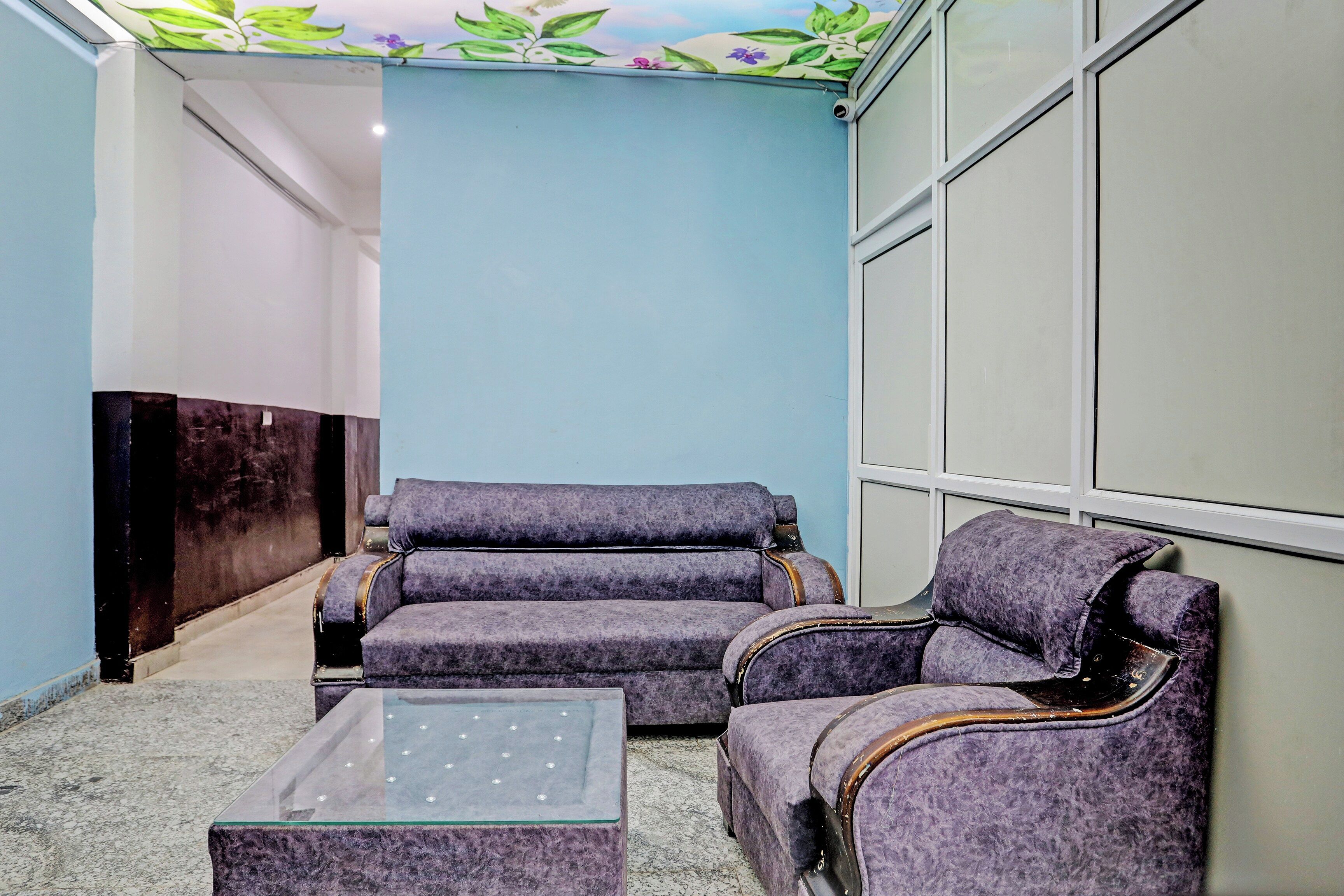A lobby with a blue wall, a dark wooden reception desk, and two purple armchairs with a glass coffee table.