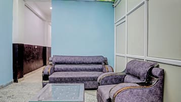 A lobby with a blue wall, a dark wooden reception desk, and two purple armchairs with a glass coffee table.