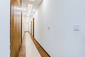 Un long couloir étroit, avec des portes en bois d’un côté et des murs blancs de l’autre.