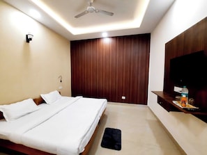 Hotelkamer met een bed, plafondventilator, houten paneelwand en een televisie op een houten plank.