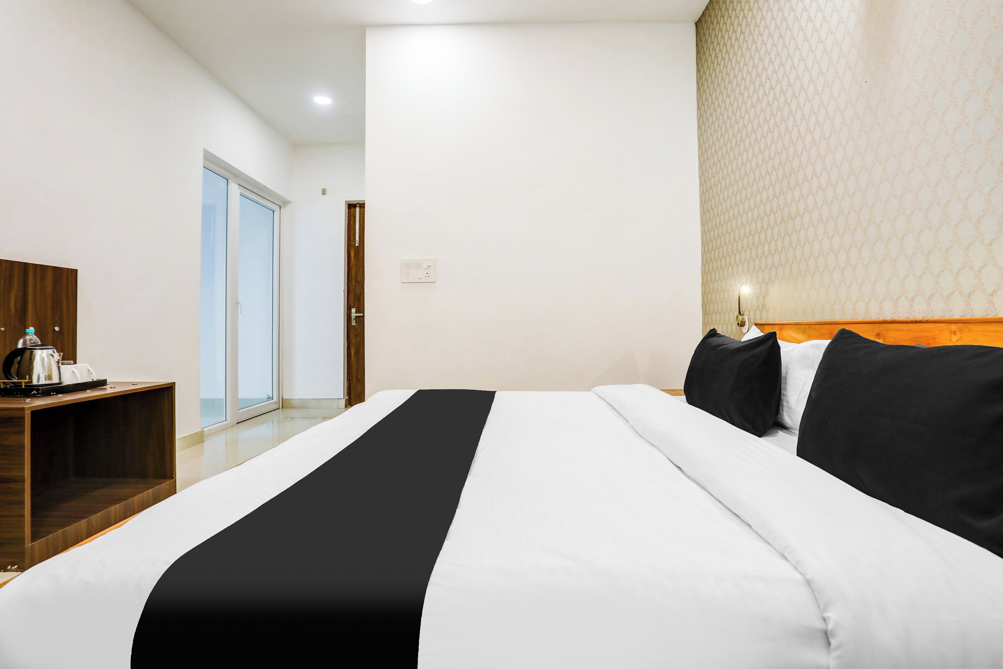 Een hotelkamer met een bed, een houten nachtkastje, een waterkoker en een behangen muur.
