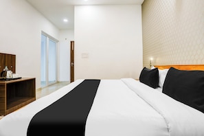 Een hotelkamer met een bed, een houten nachtkastje, een waterkoker en een behangen muur.