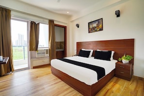 A hotel room with a large bed, a desk, a chair, a potted plant, and a painting on the wall. - Super Hotel O by OYO THE VIRAAJ BANQUET (Greater Noida)