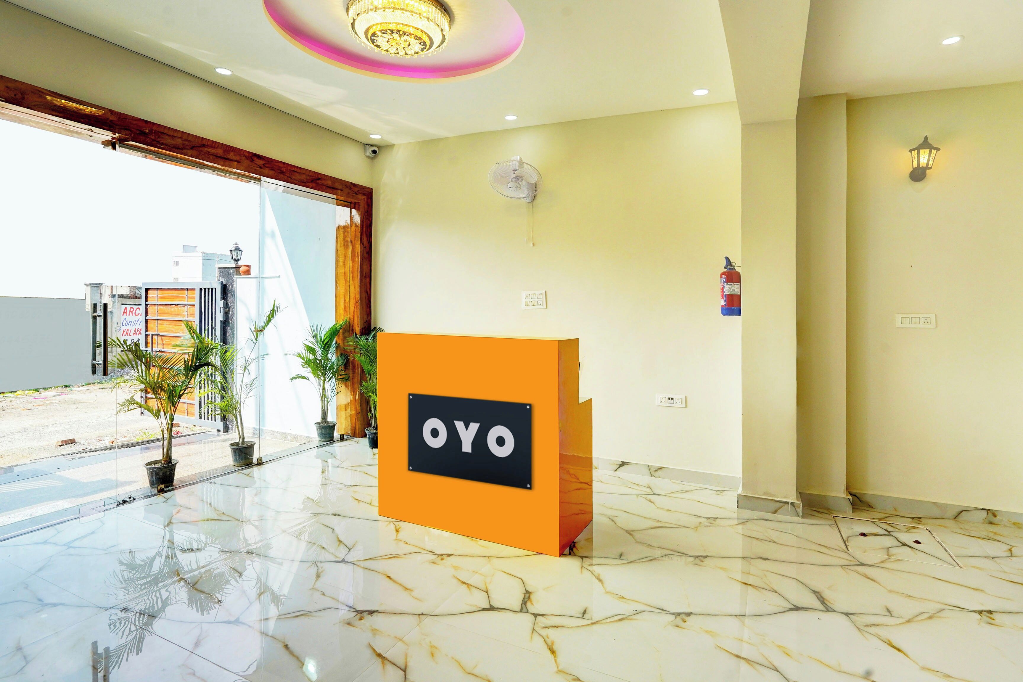 A hotel reception area with a marble floor, a reception desk labeled 'OYO,' and a fire extinguisher mounted on the wall.