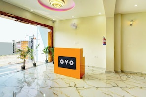 A hotel reception area with a marble floor, a reception desk labeled 'OYO,' and a fire extinguisher mounted on the wall. - Super Hotel O by OYO THE VIRAAJ BANQUET (Greater Noida)