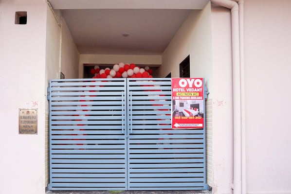 Une entrée fermée par un portail, avec une enseigne indiquant « OYO Hotel VEDANT », précisant si les chambres sont climatisées ou non, et mentionnant qu’une seule place de stationnement est disponible.