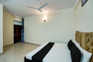 A hotel room with a bed, a ceiling fan, a wall-mounted light, and a door with a curtain.