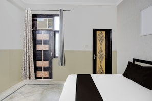 Une chambre d’hôtel comprenant un lit, une porte ornée d’un panneau décoratif, une fenêtre avec des rideaux et un mur à la finition texturée.