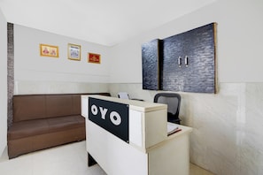A reception area with a brown sofa, a desk with a sign that reads 'OYO', and three framed pictures on the wall. - Hotel O N Nature Green (Noida)