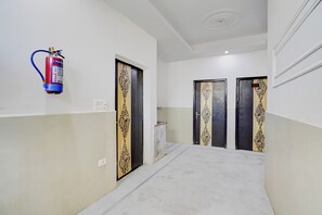 A hallway with two doors, a fire extinguisher mounted on the wall, and a tiled floor. - Hotel O N Nature Green (Noida)