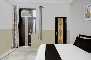 Une chambre d’hôtel comprenant un lit, une porte ornée d’un panneau décoratif, une fenêtre avec un rideau et un climatiseur fixé au mur.