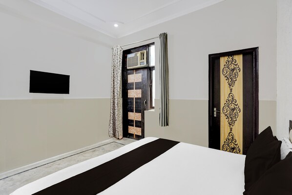 A hotel room with a bed, a door with a decorative panel, a window with curtains, and a wall-mounted television. - Hotel O N Nature Green (Noida)