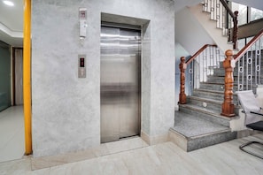 An elevator with a digital display, a staircase with wooden balusters, and a yellow pole. - Townhouse Oak Sector 63 A Noida (Noida)
