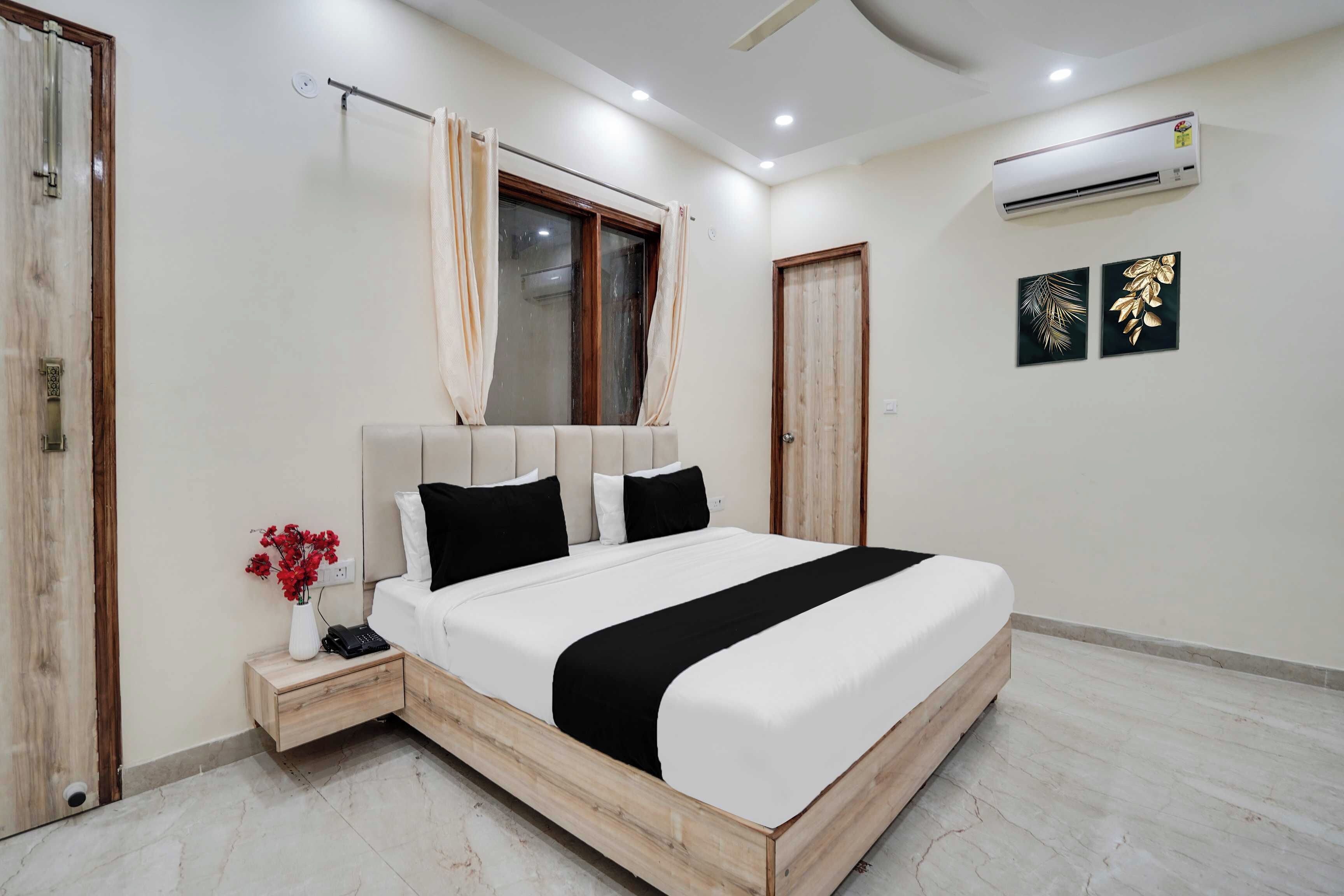 Een slaapkamer met een bed, een nachtkastje, een raam met gordijnen, een airconditioner en twee kunstwerken aan de muur.