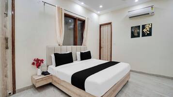 Een slaapkamer met een bed, een nachtkastje, een raam met gordijnen, een airconditioner en twee kunstwerken aan de muur.