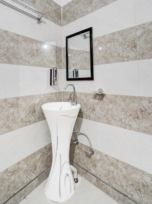 Un bany amb un lavabo de pedestal blanc, un mirall i una dutxa.