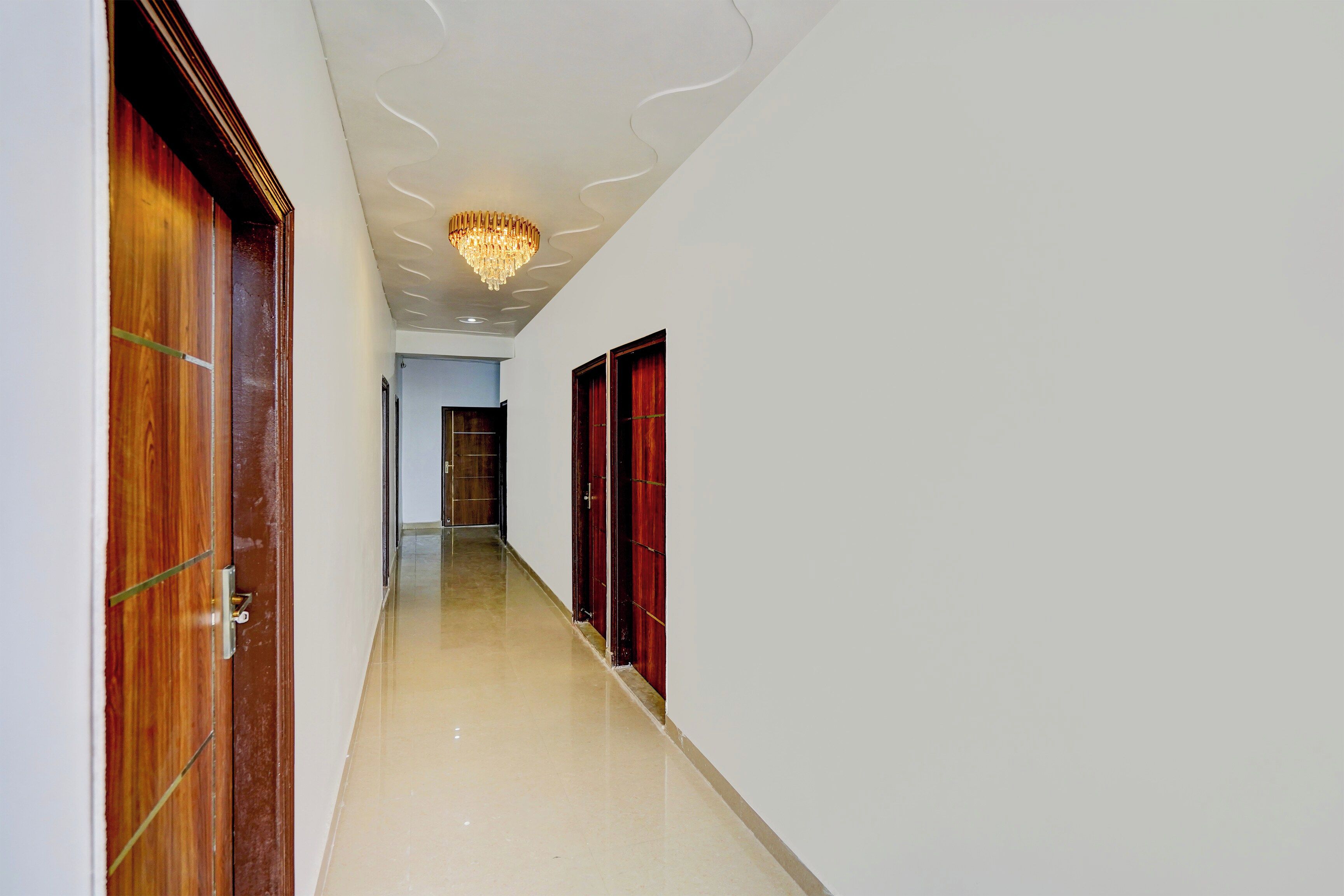 A hallway with wooden doors, a chandelier, and a tiled floor.
