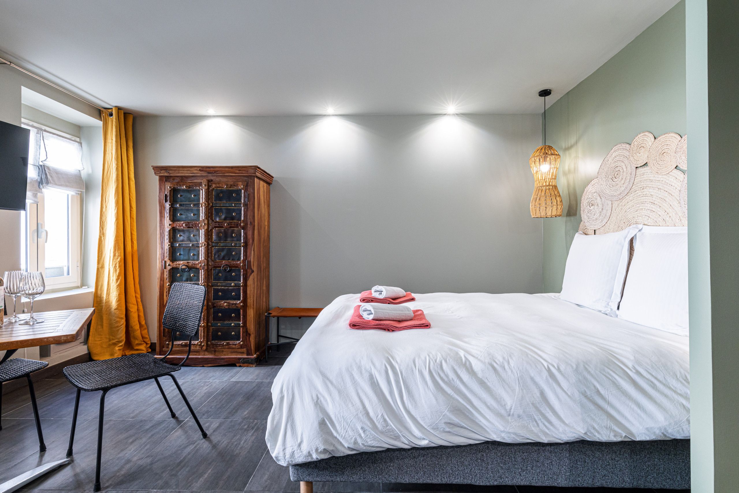 Een hotelkamer met een bed, een houten kast, een tafel met stoelen en een raam met gordijnen.