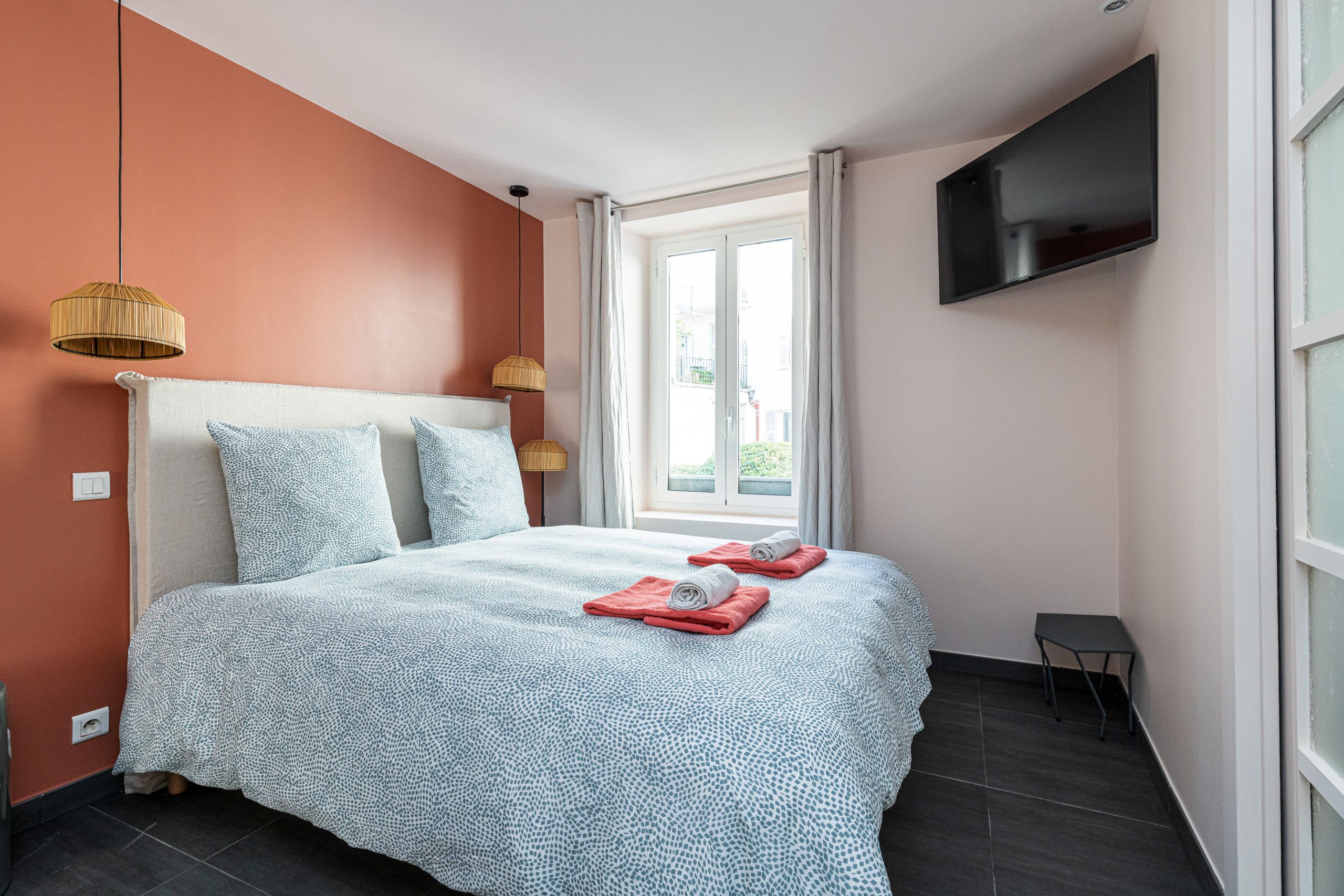 A bedroom with a bed, a television mounted on the wall, and a window with curtains.