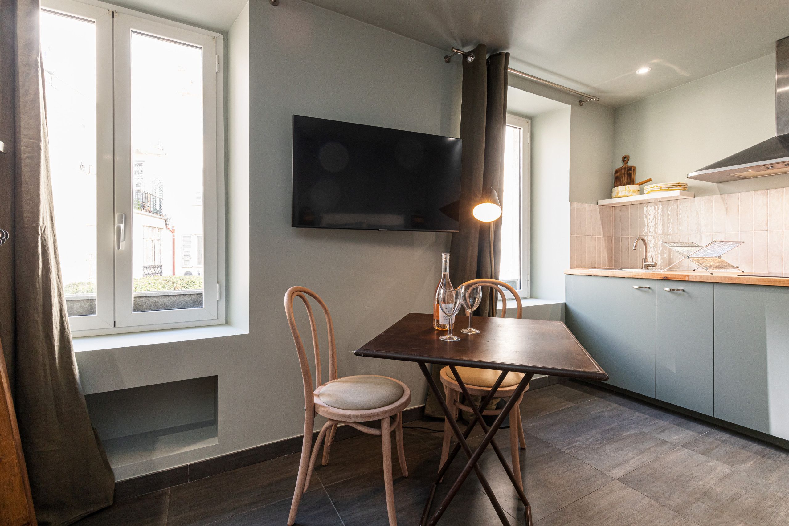 Een moderne keuken met een eettafel, stoelen, een flatscreen televisie en uitzicht naar buiten.