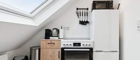 A compact kitchen with a skylight, a stove, a microwave, and a refrigerator.