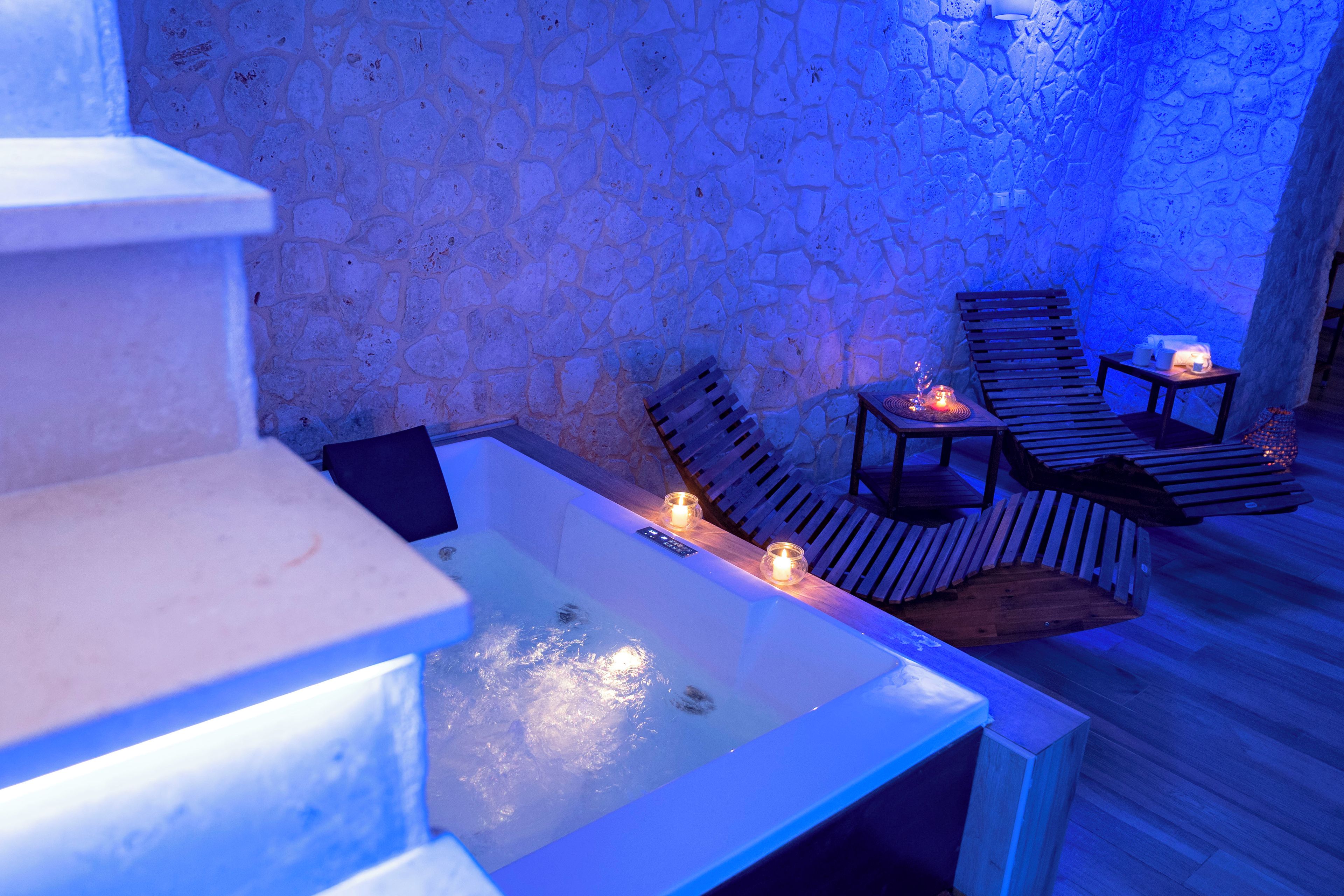 Una stanza con pareti in pietra, una piscina, poltrone da relax in legno e candele.