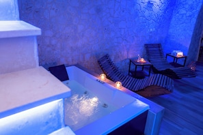 A stone-walled room with a pool, wooden lounge chairs, and candles. - Piazza Vecchia SUITE & SPA (Castellana Grotte)