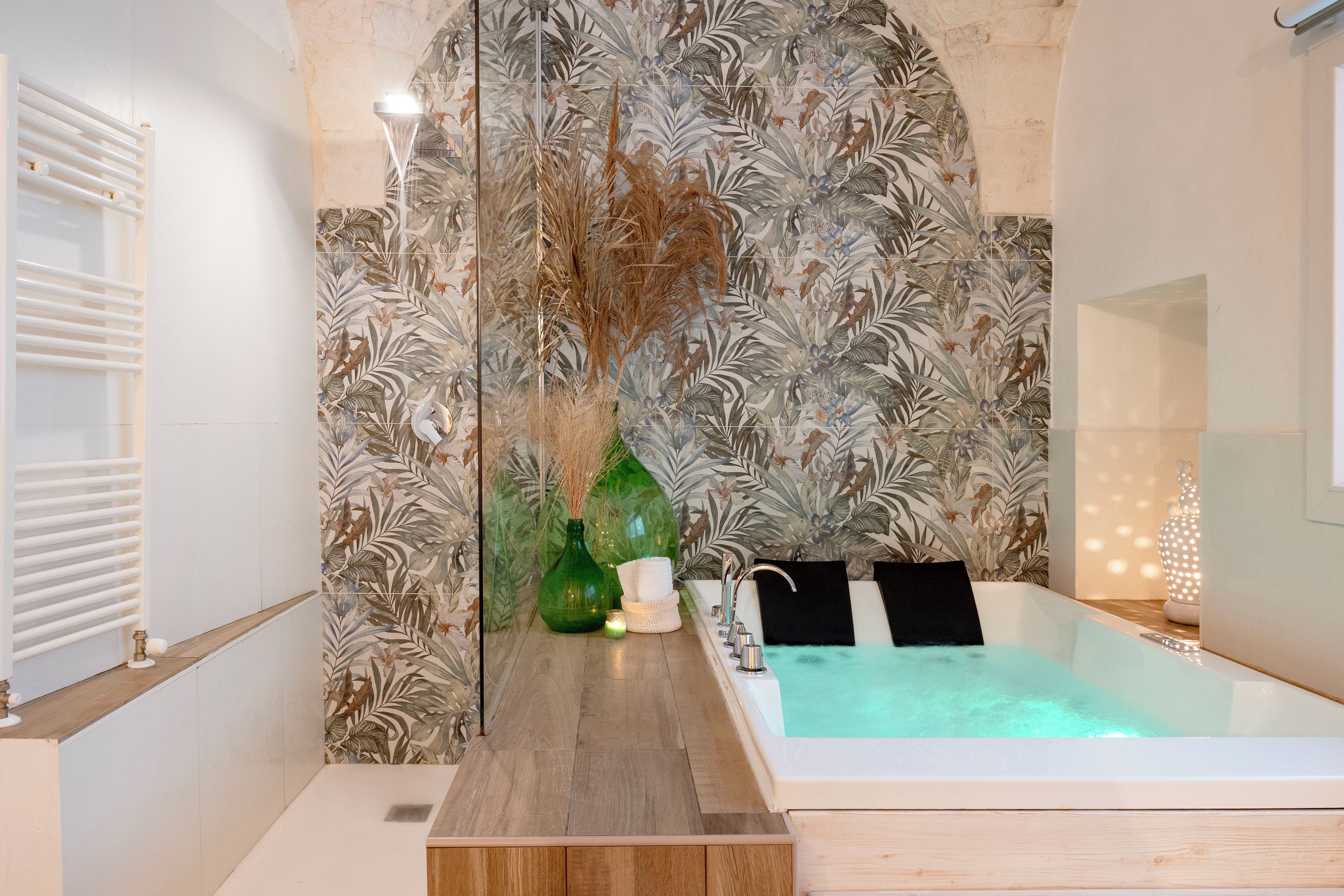 Un baño moderno con una bañera grande, un tocador de madera y una pared decorativa con un diseño de hojas tropicales.