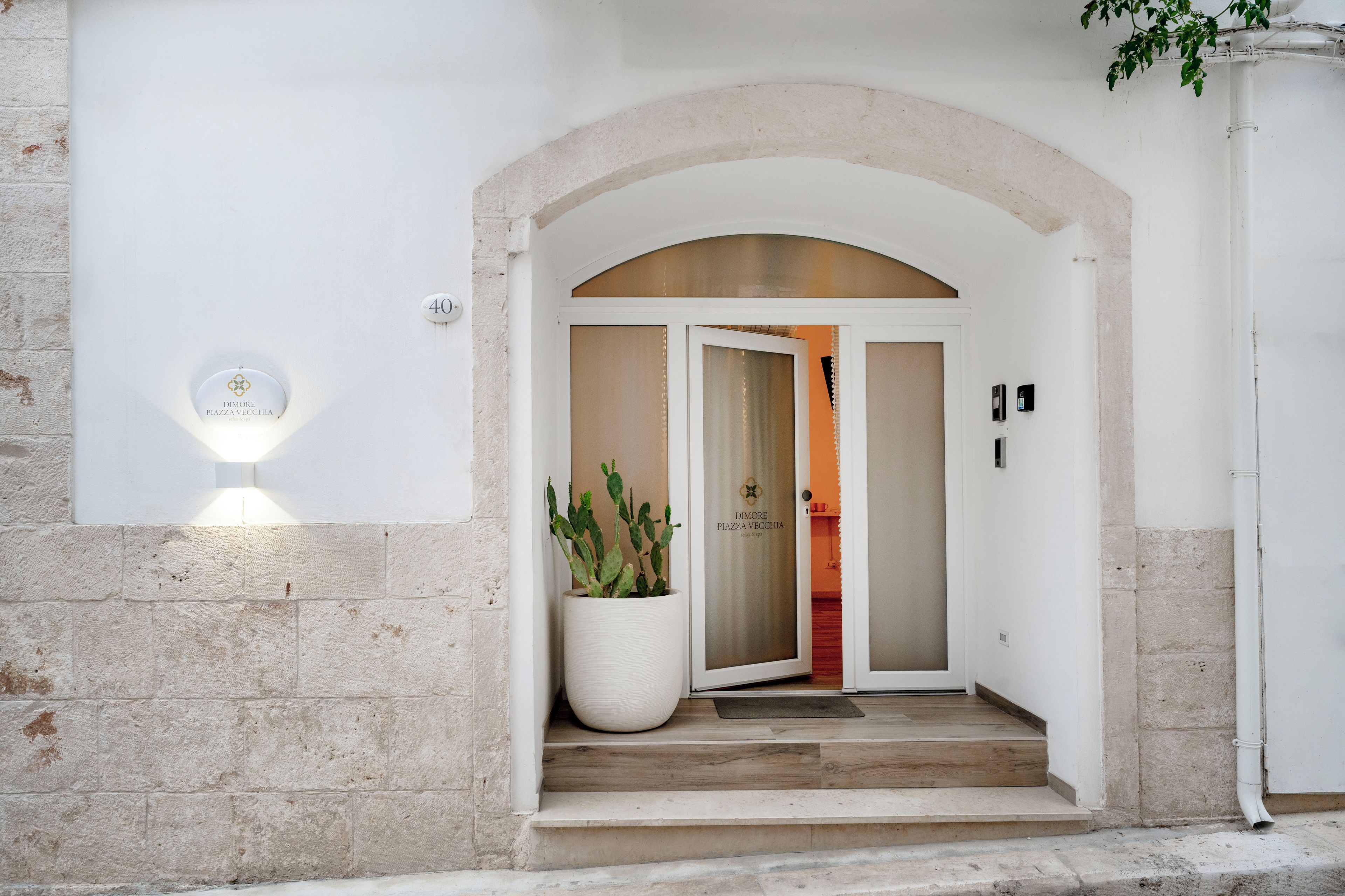 L’entrée d’un hôtel, avec une façade en pierre, un grand pot de fleurs et une porte dotée d’un panneau en verre.
