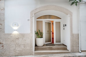 A hotel entrance with a stone facade, a large potted plant, and a door with a glass panel. - Piazza Vecchia SUITE & SPA (Castellana Grotte)