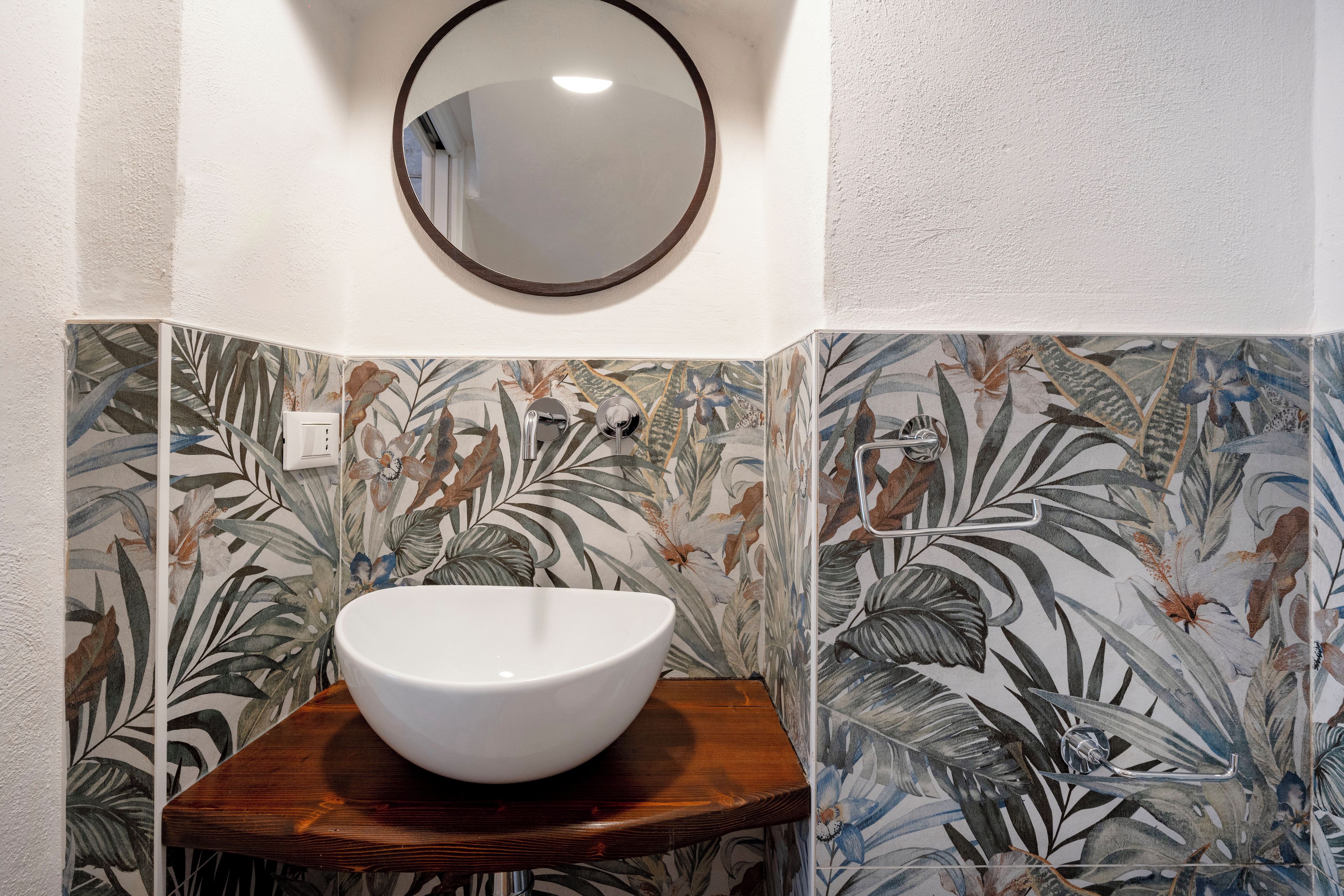 A bathroom with a white sink on a wooden stool, surrounded by floral patterned tiles.