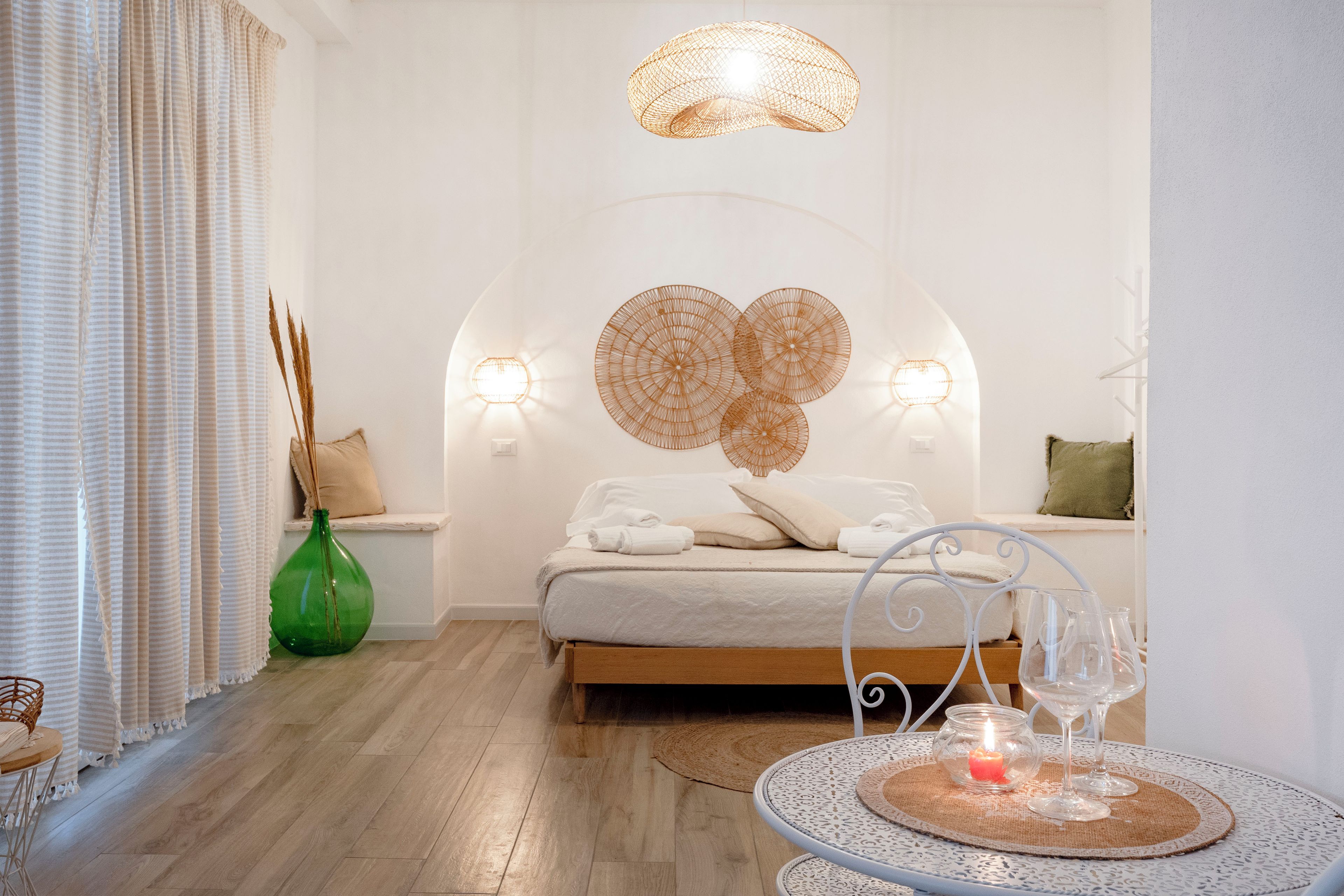 Une chambre d’hôtel avec un lit, des lampes de chevet, un élément décoratif mural, un vase vert et une petite table ronde avec une bougie et des verres.