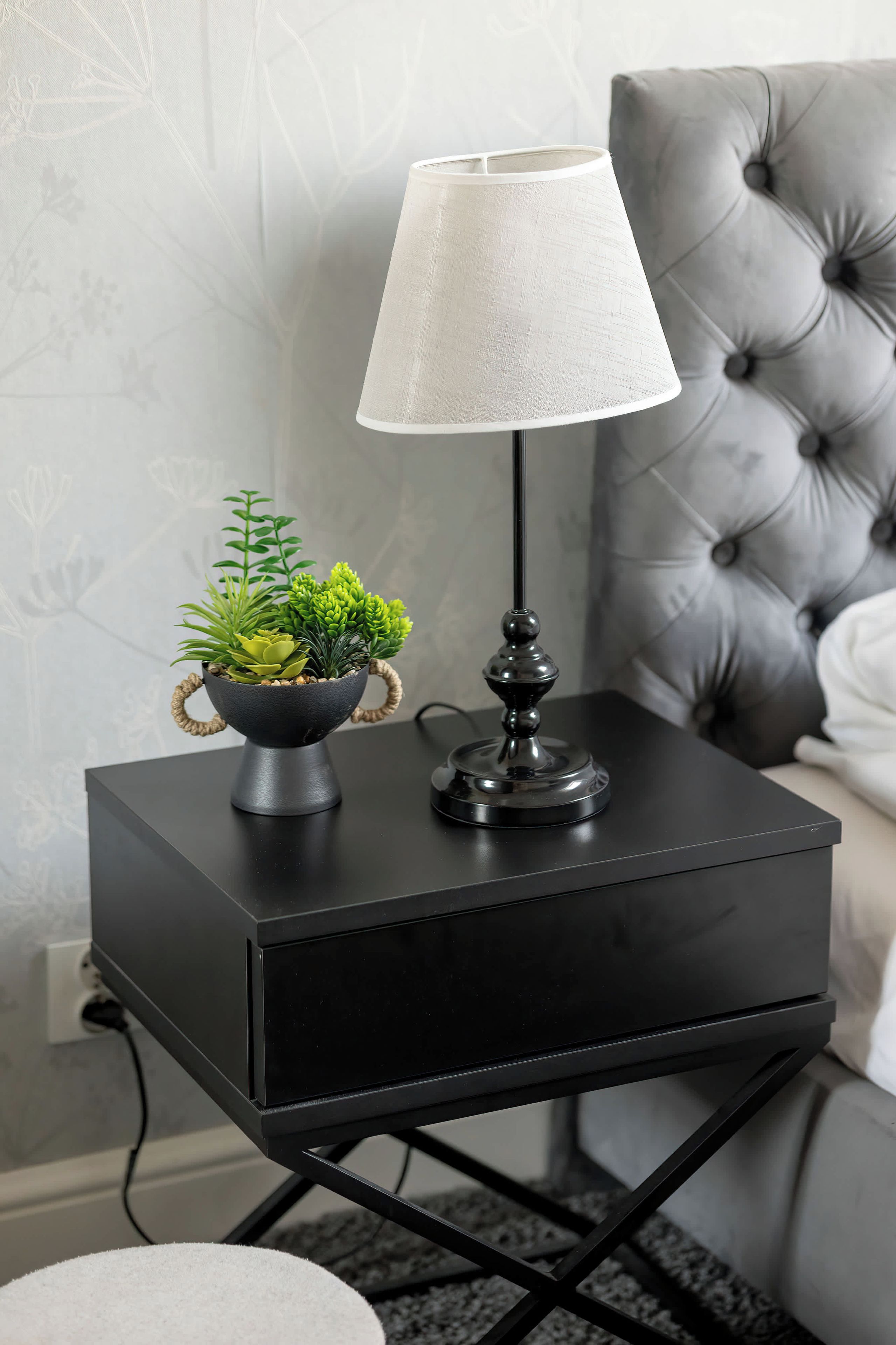 A black bedside table with a lamp and a small plant.