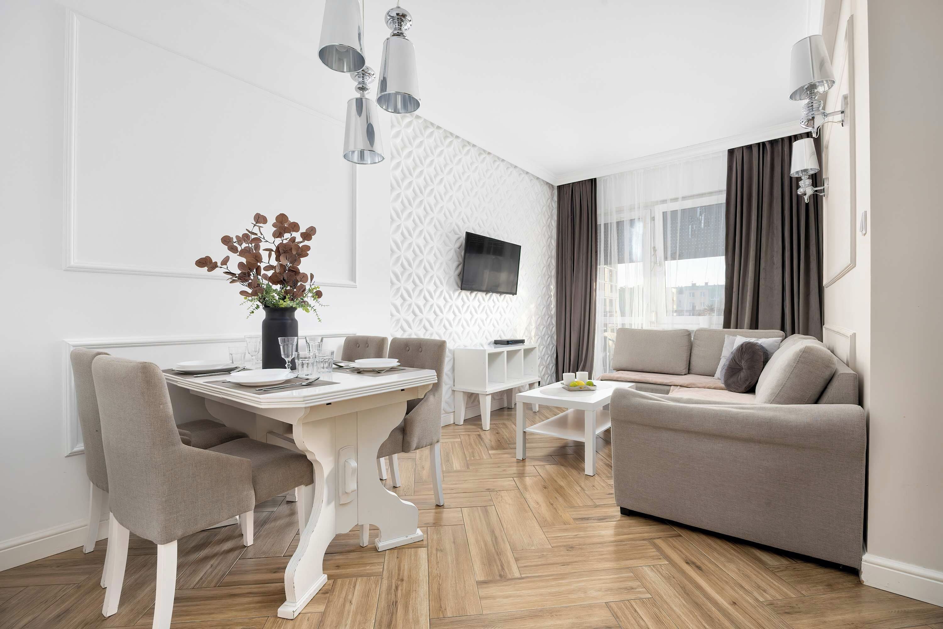 A modern living room with a dining area, a sofa, a TV mounted on the wall, and a window with curtains.