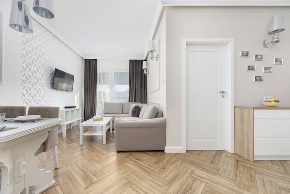 A modern living room with a sofa, a dining table, and a TV mounted on the wall. - Kielce | Warszawska 218E | Spacious Apartment | Workspace (Kielce)
