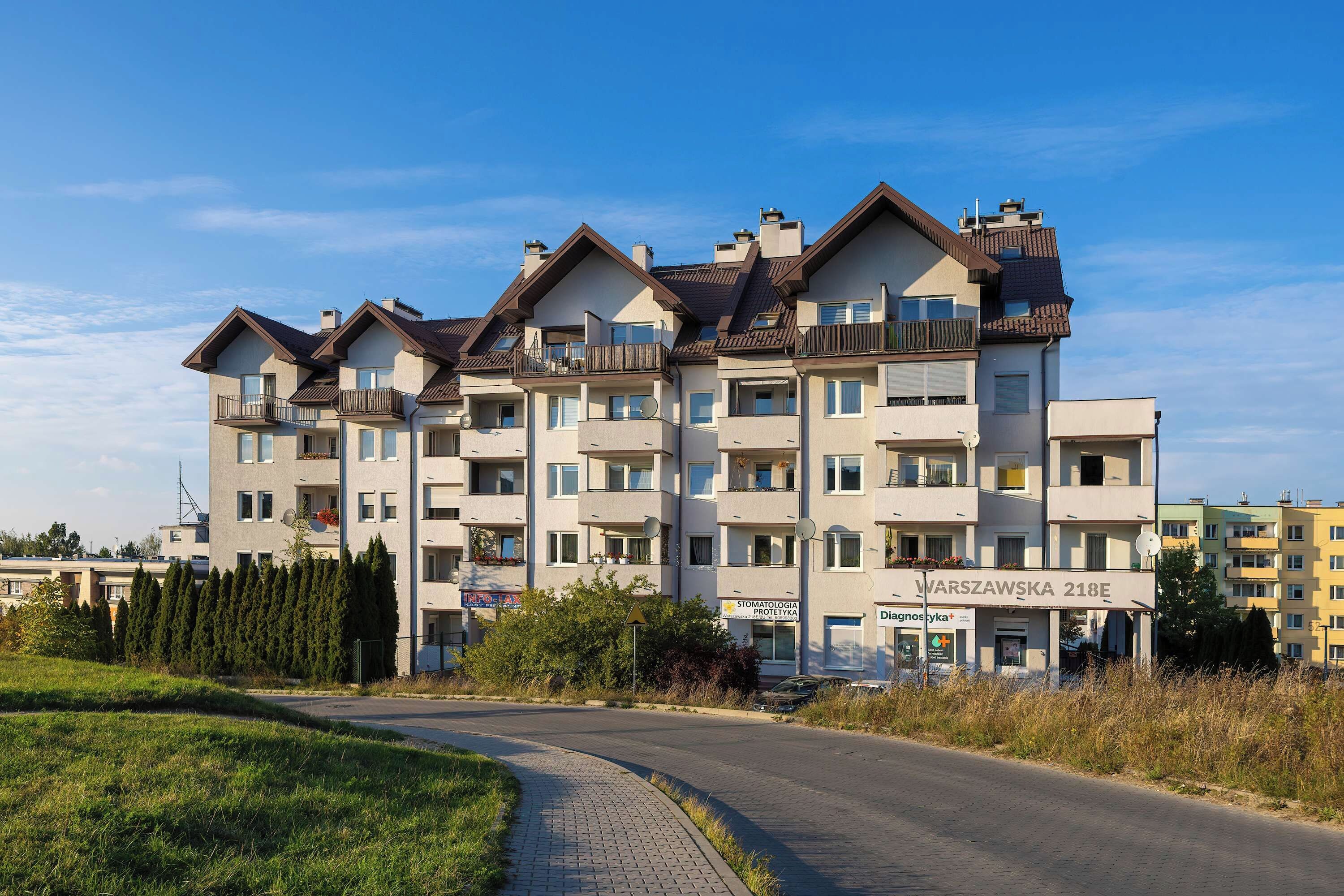 A multi-story residential building with balconies, a paved driveway, and a clear sky.