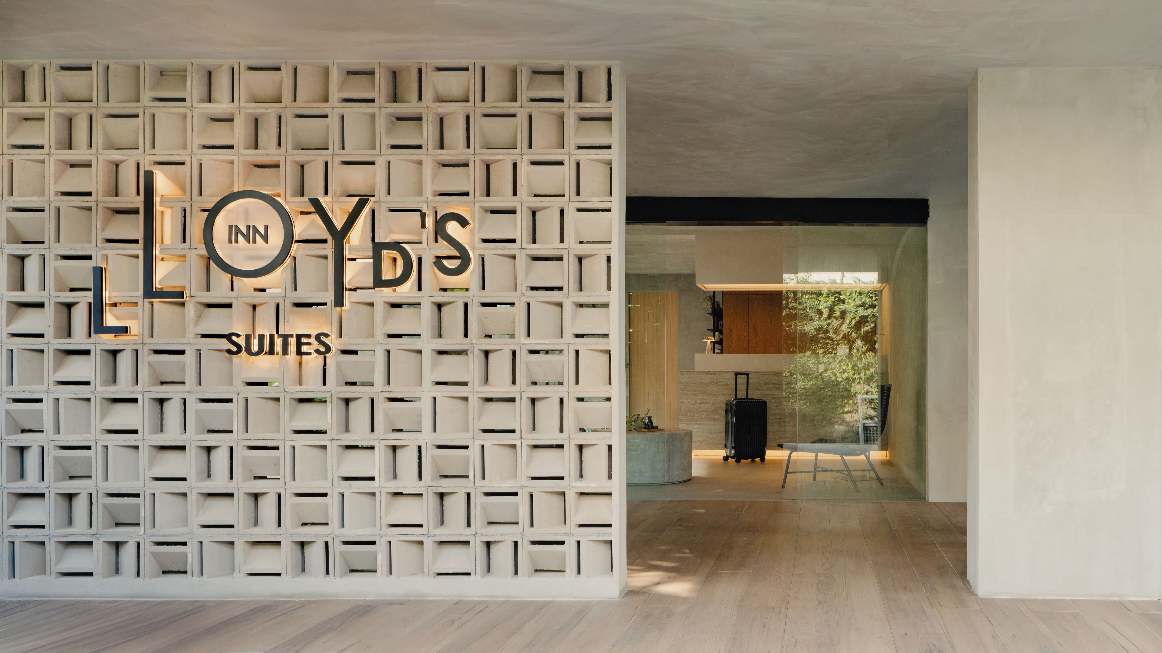 Entrada de un hotel con un diseño geométrico en la pared y el nombre 'LOYS SUITES' iluminado.