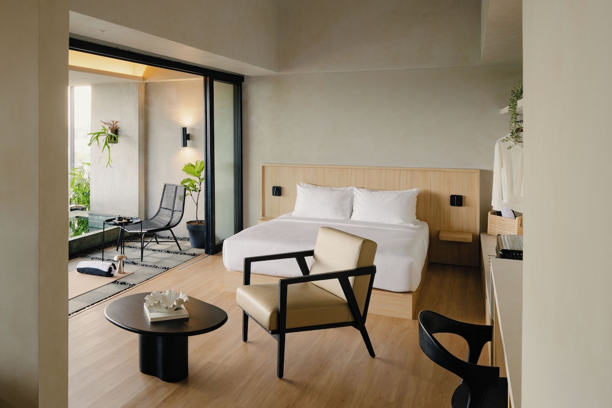 Habitació d'hotel moderna amb un llit, dues cadires, una taula petita i vista a l'exterior.
