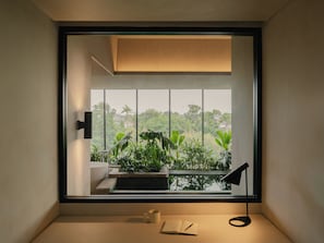 A room with a large window, a desk with a lamp, a notebook, and a mug. - Lloyd's Inn Suites (Seminyak)