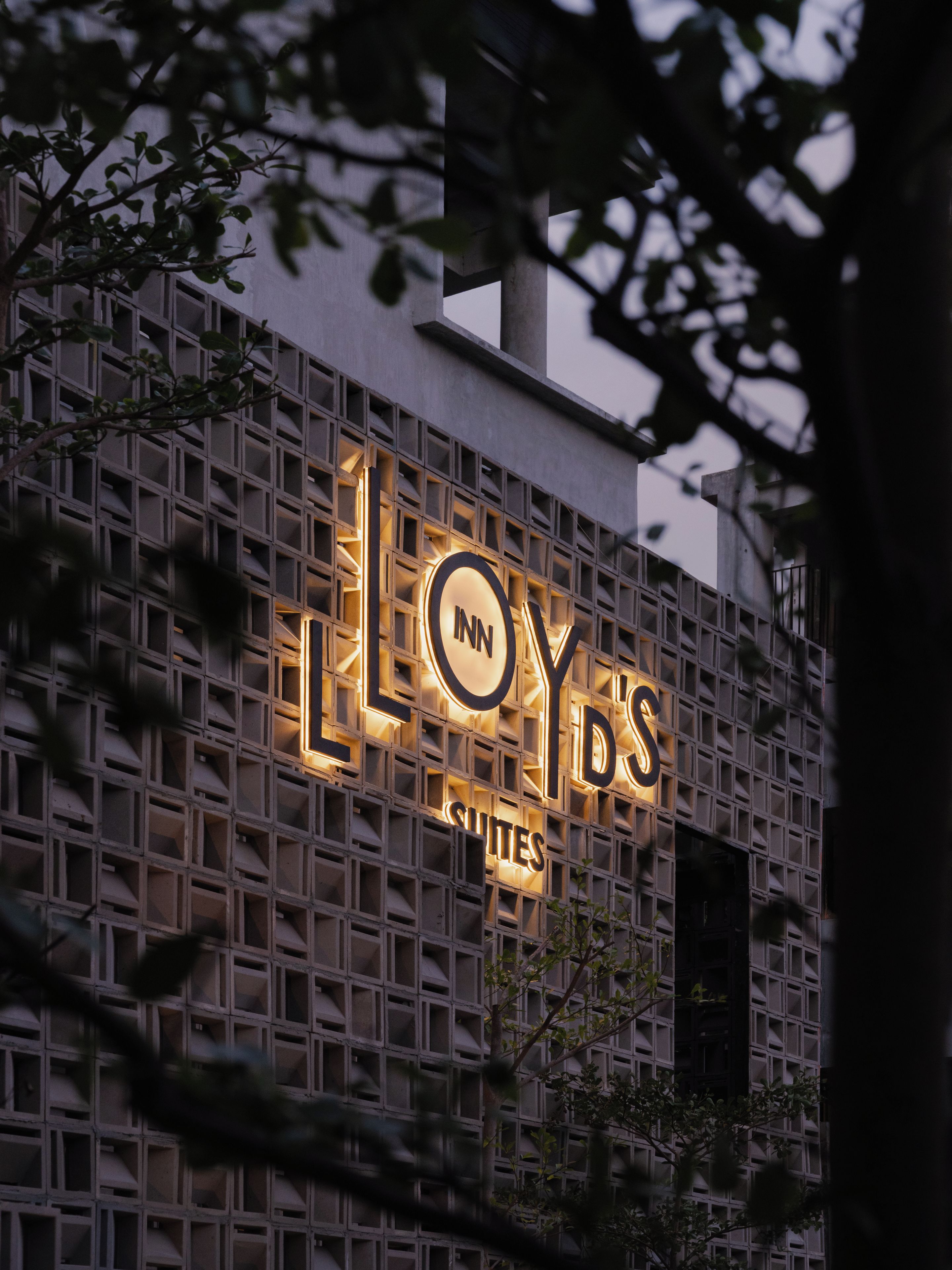 Fachada de edificio con un diseño de cuadrícula y letreros iluminados que dicen 'LLOYDS SQUITES'.